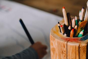 child writing in background-pot of pencils in foreground